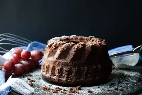 En saftig sockerkaka choklad, pudrad med florsocker, med vindruvor och visp i bakgrunden.