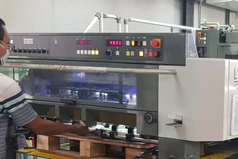 Operator w maszynie drukarskiej Komori Lithrone A37 z panelem sterowania i wyświetlaczem.