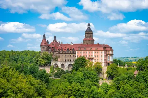 Imponujące pałace w Polsce, jak ten z czerwonym dachem i wieżami, otoczone bujną zielenią, kuszą historią i baśniowym klimatem.