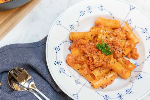 En tallrik med krämig pasta alla zozzona, toppad med persilja och svartpeppar. Bredvid ligger en servett och bestick.