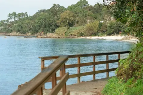 Camino de madera hacia la playa Mogor, con el mar azul y la costa verde al fondo.