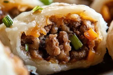 Pyszne pierogi z mięsem, z widocznym farszem i zieloną cebulką, kuszą apetycznym wyglądem.