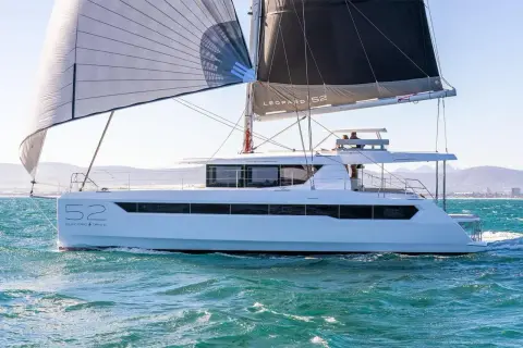 Un catamarano Leopard 52 con vele spiegate naviga su acque turchesi, con montagne sullo sfondo.