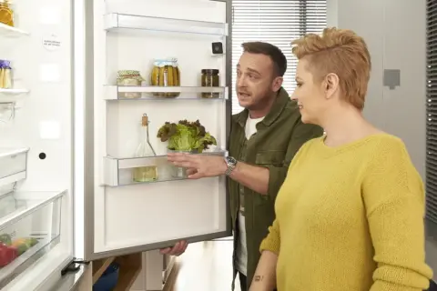 Para wybrać jaką lodówkę wybrać, para ogląda wnętrze z sałatą i przetworami.