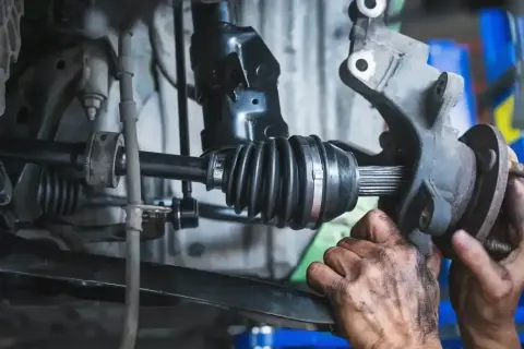Mechanik sprawdza przegub zewnętrzny w samochodzie. Widać gumową osłonę i metalowe elementy.