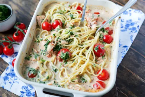 Herzhafte Lachs Spinat Pasta in cremiger Sauce mit Kirschtomaten, serviert in einer Auflaufform.