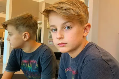 Ragazzo con taglio capelli bambino 11 anni, capelli biondi sfilati e ciuffo. Riflesso nello specchio.