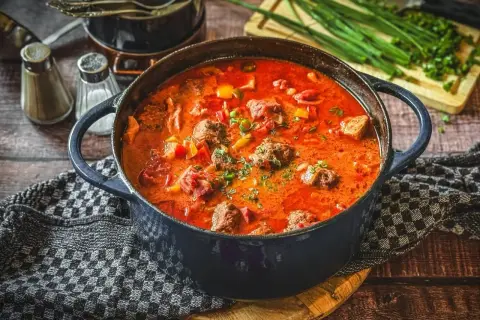 Herzhaftes Pfundstopf Rezept in einem Gusseisentopf, mit Fleischklößchen, Paprika und einer würzigen Tomatensoße, garniert mit frischen Kräutern.