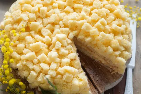 Una deliziosa torta mimosa, ricoperta di soffici briciole di pan di Spagna, con un rametto di mimosa a decorare.