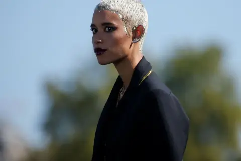 Mujer con pelo blanco corto y maquillaje dramático, luciendo un pendiente llamativo en la oreja.
