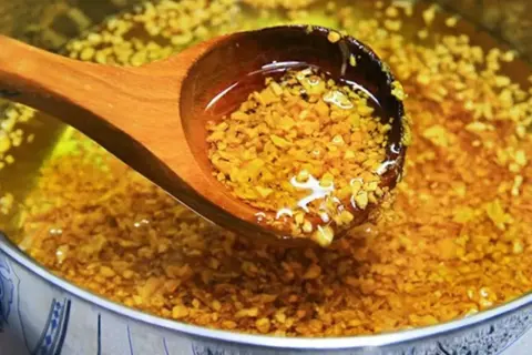 Holzschöpfkelle hebt goldbraun angebratenen Knoblauch aus heißem Öl. Knoblauch anbraten oder nicht? Hier die Antwort!