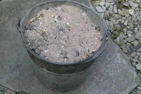 Metalowy kubeł wypełniony popiołem z węgla, który może posłużyć jako cenny nawóz do ogrodu.
