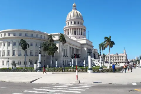 Majestatyczny Kapitol w Hawanie, otoczony palmami, pod błękitnym niebem. Spacerujący ludzie i klasyczna architektura tworzą obraz kubańskiego dnia.
