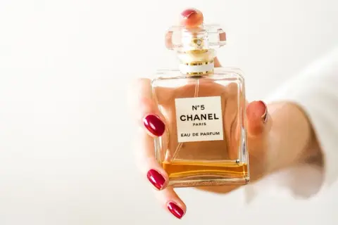 Dłoń z czerwonymi paznokciami trzyma flakon Chanel N°5. Czy perfumy mają datę ważności?