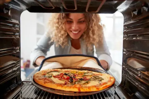 Kobieta wyjmuje z piekarnika pyszną pizzę. Idealna temperatura do pieczenia pizzy to klucz do sukcesu.