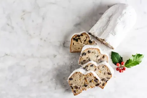 Le stollen, un délice de Noël, est saupoudré de sucre glace. Des tranches révèlent des fruits secs et des baies rouges sur une branche de houx.