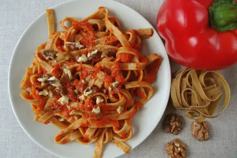 Pyszne spaghetti z papryką i orzechami włoskimi, obok czerwona papryka i surowy makaron.