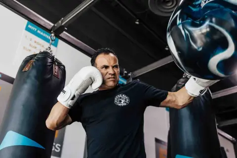 Man with intense focus, performing boxing workouts at home with a heavy bag. He wears white gloves and a black t-shirt.