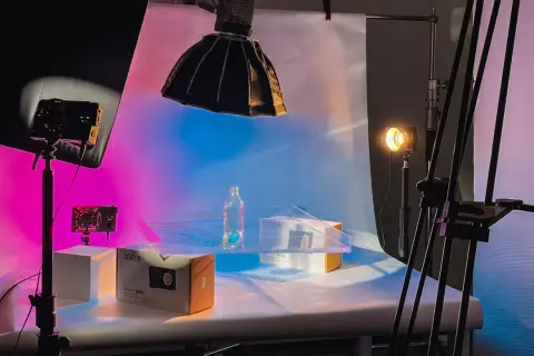 Product photography setup with a bottle and boxes on a table, illuminated by colorful background light and studio lights.
