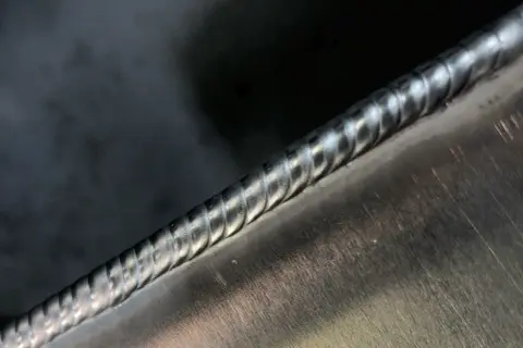 Precyzyjne spawanie aluminium migomatem. Widoczny gładki, lśniący ścieg spawalniczy na metalowej powierzchni.
