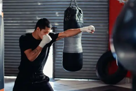 A boxer trains in a gym, practicing the sweet science of boxing with a punching bag.