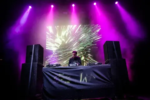 DJ na scenie, fioletowe światła, wizualizacje na ekranie. Sprawdź audioriver timetable, by nie przegapić jego występu!