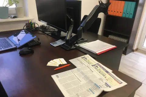 Biurko z laptopem, monitorem, kalkulatorem, gazetą "Gazeta Podatkowa" i wizytówkami.