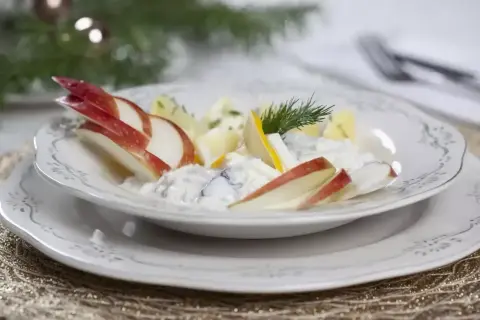 Pyszne śledzie w śmietanie z jabłkiem i koperkiem, podane na eleganckim talerzu, idealne na świąteczny stół.