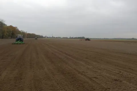 Traktory pracują na polu, przygotowując ziemię. Widać ślady po maszynach, które pomagają w obliczeniu hektara przeliczeniowego.