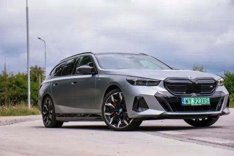 Srebrne BMW i5 na tle pochmurnego nieba, z widocznymi felgami i tablicą rejestracyjną.
