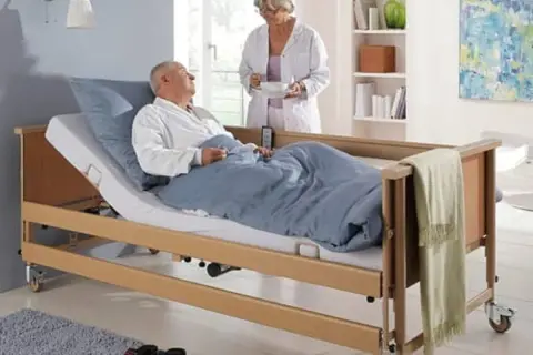 Opieka nad chorym członkiem rodziny: pielęgniarka podaje posiłek leżącemu w łóżku pacjentowi.