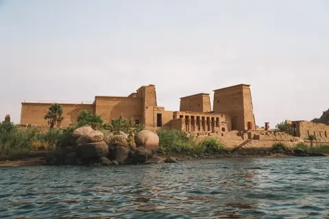 Antiguo templo egipcio en una isla, con el Nilo en primer plano. La imponente arquitectura de la presa de Asuán se alza majestuosa.