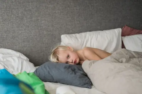 Ett litet barn med stora halsmandlar ligger i en säng, ser trött ut.
