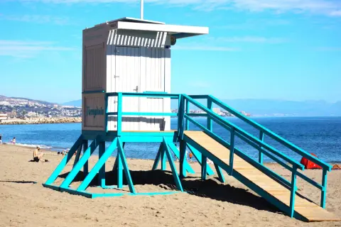 Ratownik na plaży w Fuengiroli, jedna z atrakcji Costa del Sol. Błękitna konstrukcja i biała budka ratownicza na tle morza i gór.