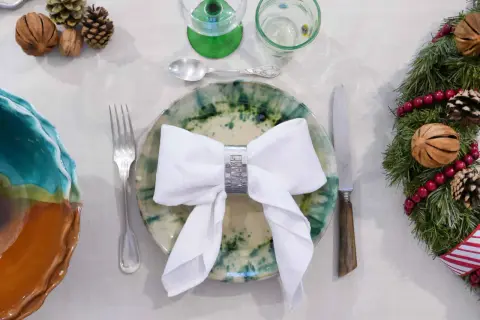 Une table dressée pour Noël avec un pliage serviette robe élégant, des pommes de pin et une guirlande festive.