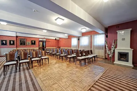 Elegancka sala konferencyjna w Lanckorona Hotel Modrzewiówka, z rzędami krzeseł, portretami na ścianach i ozdobnym piecem.