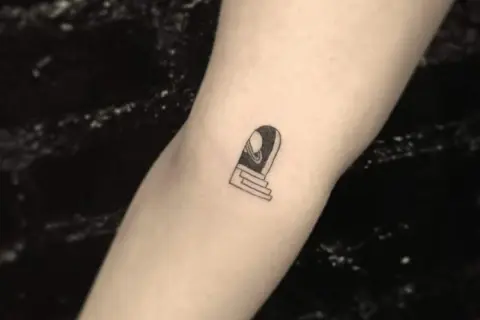 Ein kleines Tattoo auf dem Arm eines Mannes zeigt eine Tür mit Stufen, die zu einem Planeten führt.