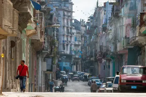 Photographie de rue d'une rue cubaine animée, avec des bâtiments colorés et délabrés, des voitures anciennes et un homme marchant seul.