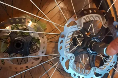 Dwa hamulce tarczowe rowerowe, jeden z mocowaniem center lock Shimano, drugi z mocowaniem center lock DT Swiss.