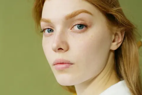 Rostro de mujer joven con pecas y ojos azules. Su cabello es pelirrojo. ¿Glicación qué es? Podría afectar la piel.