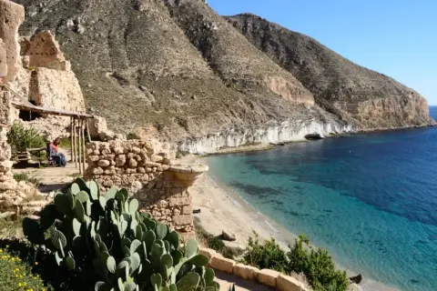 Ruinas de la hippie comuna Cala San Pedro, Almería, con mar turquesa y montañas.