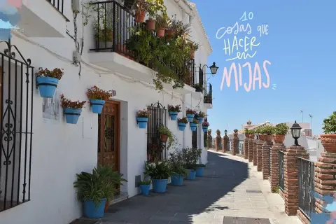 Calle empedrada con casas blancas adornadas con macetas azules y flores. Un camino perfecto para descubrir qué ver en Mijas en una tarde.