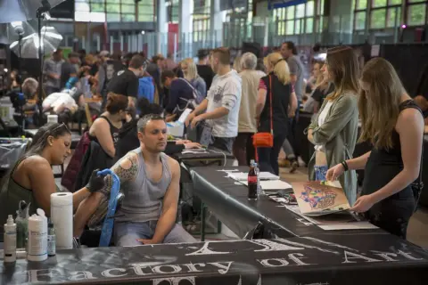 En la convencion tattoo barcelona, un artista tatúa un brazo mientras otros observan diseños.
