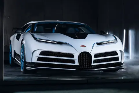 Biały Bugatti Centodieci z niebieskimi akcentami i felgami, otoczony mgłą i pionowymi światłami.