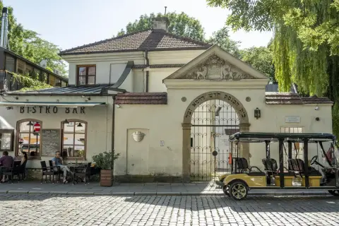 Urokliwy dzień w dzielnicy Kazimierz w Krakowie. Przy bistro barze siedzą ludzie, a obok bramy z hebrajskimi napisami stoi żółty meleks.
