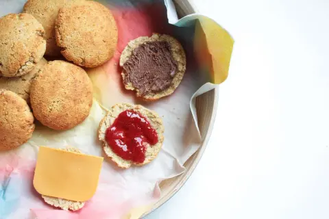 Scones med keso, chokladpålägg och sylt på en bricka. En skiva ost ligger på en scone.