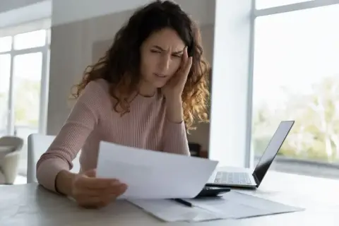 Zmartwiona kobieta analizuje dokumenty, rozważając odrzucenie spadku.