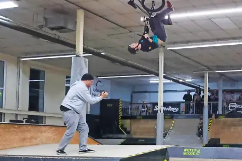 BMX-Fahrer vollführt einen Salto in der Luft in der Wicked Woods Wuppertal. Ein Mann filmt den Stunt.