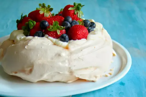 Deliciosa pavlova receta original, coronada con fresas y arándanos frescos, sobre una base de merengue crujiente y crema batida.