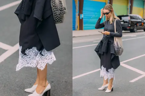 Elegancka koronkowa spódnica stylizacje z czarną marynarką i siatkową torbą. Kobieta w okularach przeciwsłonecznych i szarej bluzce z długim rękawem.